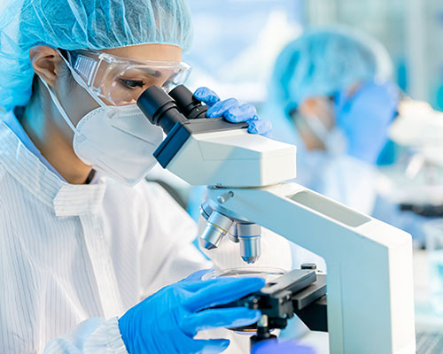 lab worker in PPE looking through microscope